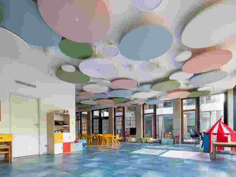 Free-hanging acoustic panels in pastel colours in large room in children's centre with colourful furniture and big windows