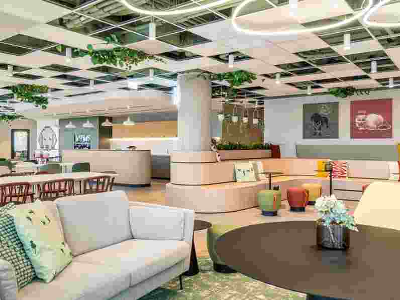 Bílý, akustický podhled s integrovanými závěsnými rostlinami ve velkém barevném kancelářském společenském prostoru. Akustické nástěnné panely s tištěnými motivy zvířat.