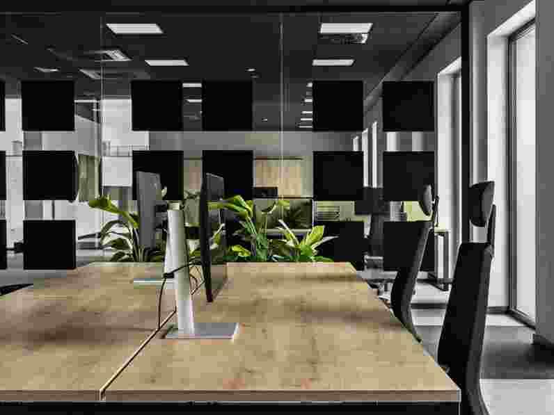 Černý, celoplošný akustický podhled v otevřené kanceláři se skleněnými stěnovými přepážkami s černými detaily a detailním záběrem pracovní stanice s dřevěnými stoly.