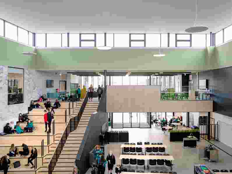 Light-green acoustic wall panels in large, spacious high school atrium with students sitting and walking in the main staircase