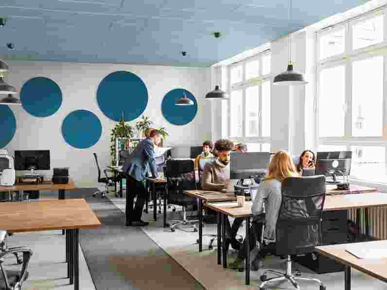 Blue acoustic wall panels in circular shape in open-plan office with people working at their desks and talking to each other